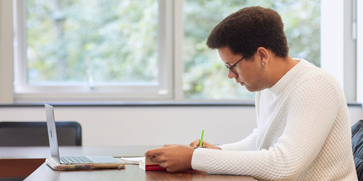 A student working on a laptop with a book.