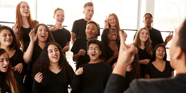 A choir, lead by the choirmaster in the foreground, at rehearsal.